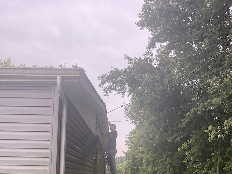 Electrician on a ladder working a service line at the roofline during a storm power-outage call
